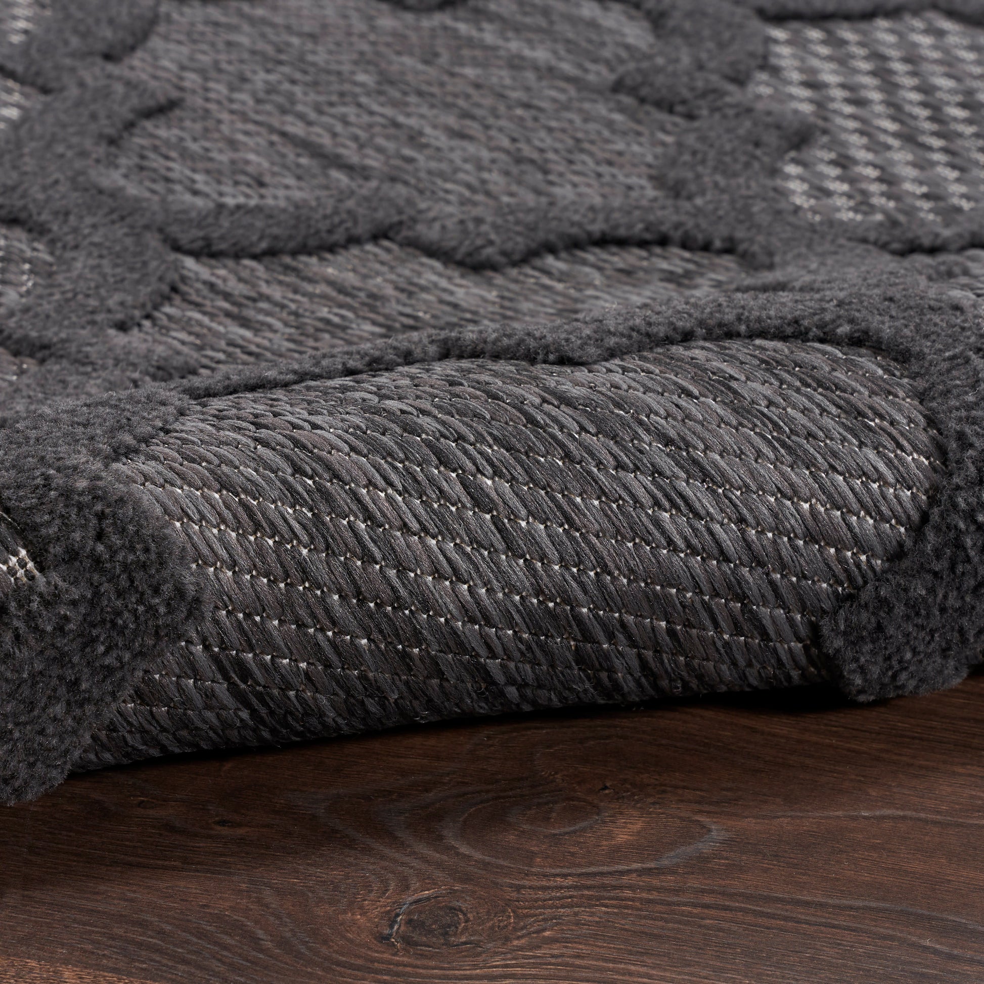 Close-up of charcoal gray textured rug with thick looped pile and soft raised border on dark wooden floor.