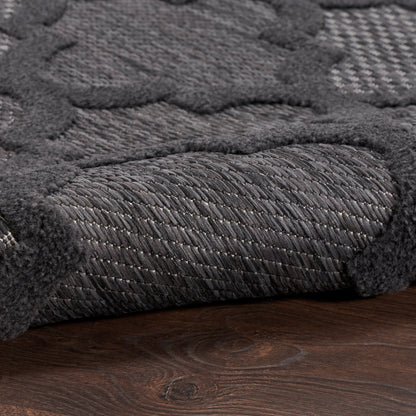 Close-up of charcoal gray textured rug with thick looped pile and soft raised border on dark wooden floor.