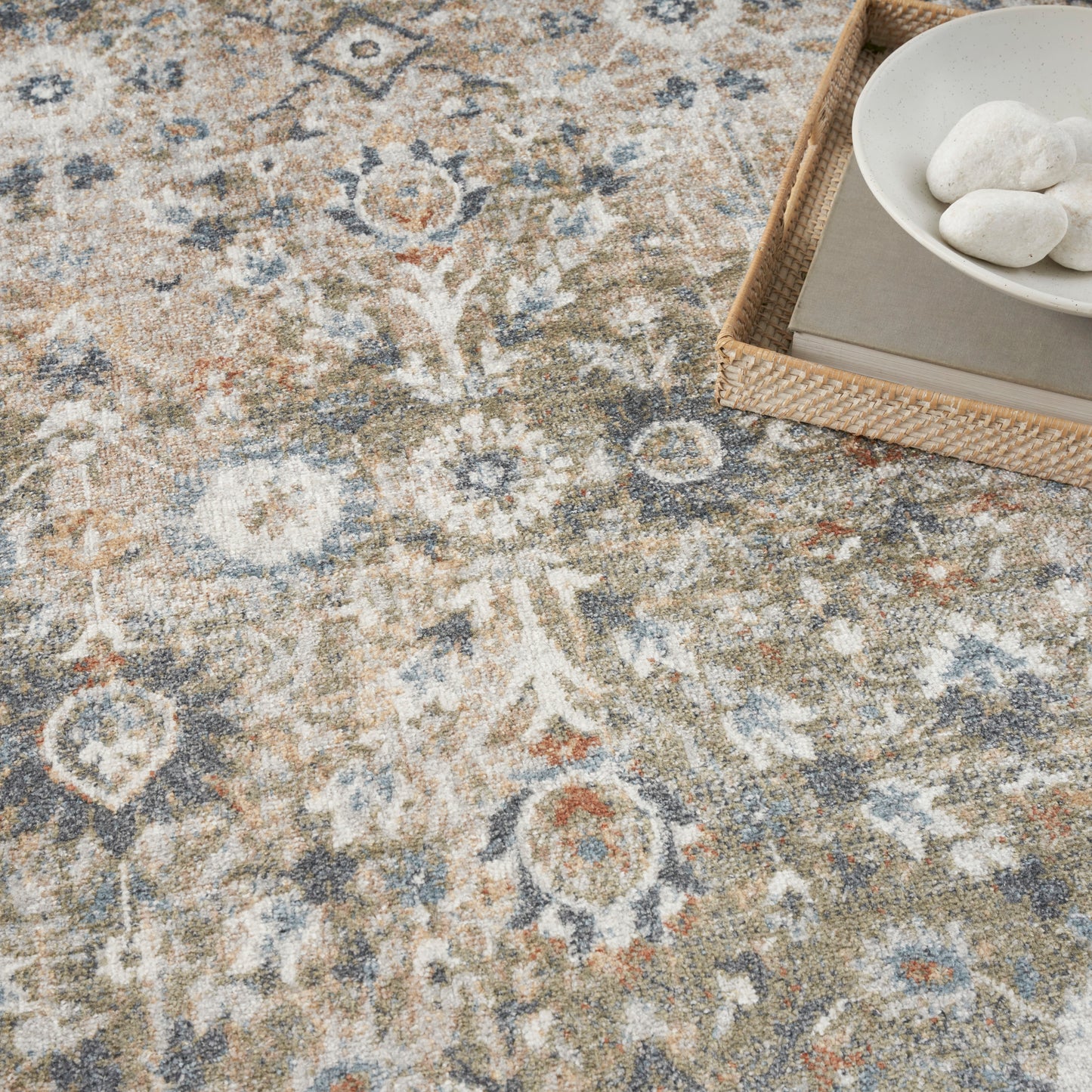 Neutral patterned area rug in blue, beige and gray; wicker tray with a white bowl and smooth stones in the corner.