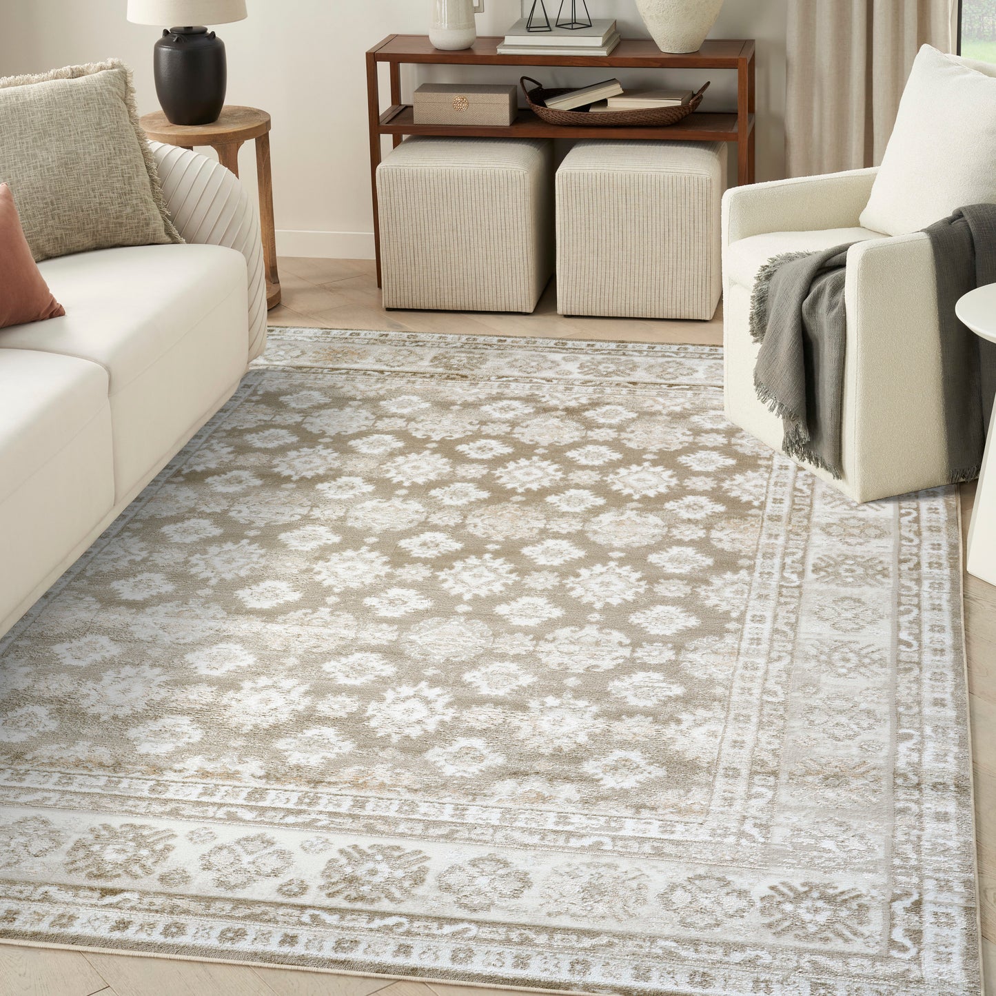 Rectangular ivory-gray ornate patterned area rug with border in a cream living room with white sofa and beige armchair.