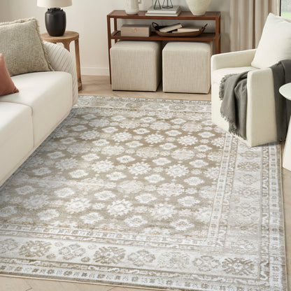 Rectangular ivory-gray ornate patterned area rug with border in a cream living room with white sofa and beige armchair.