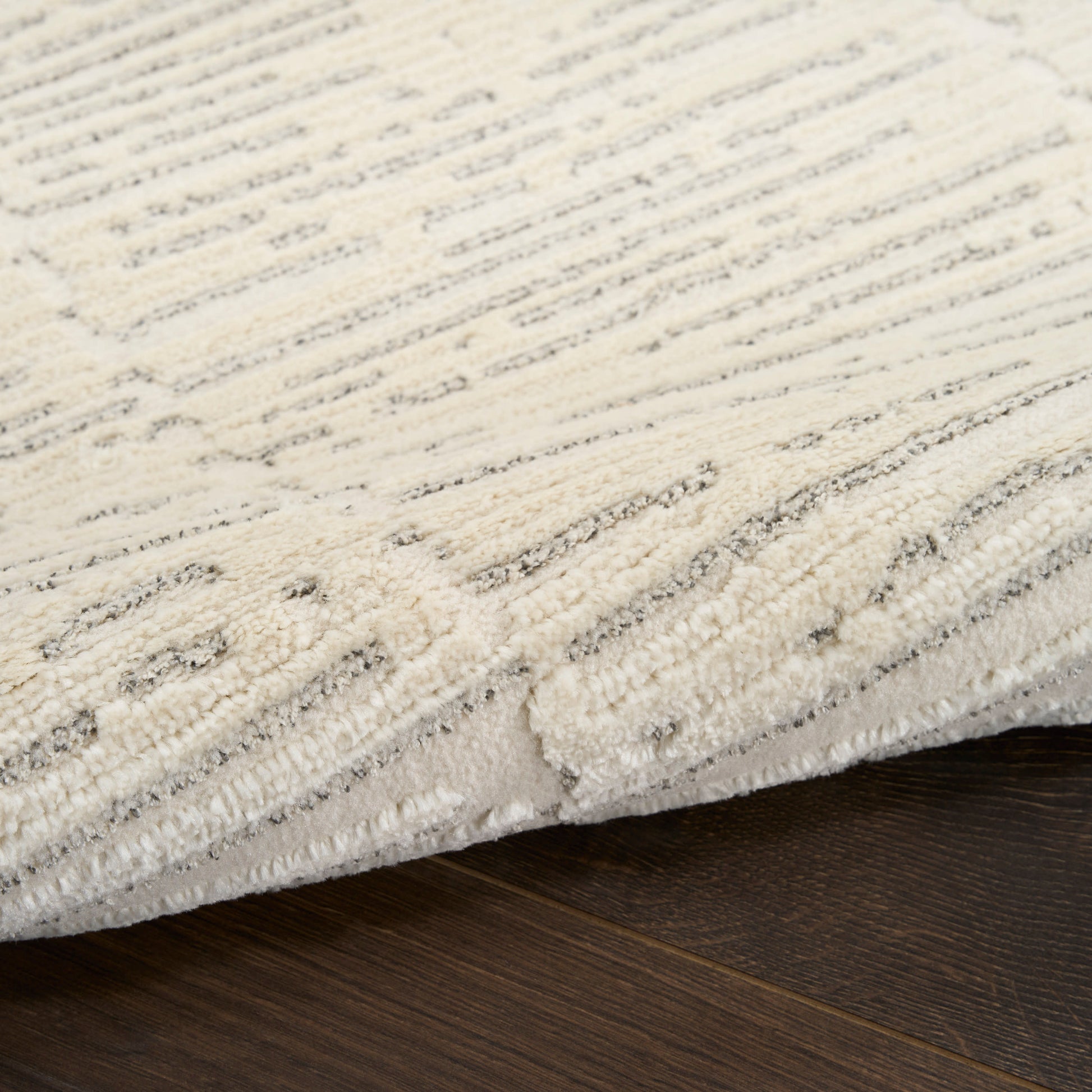 Ivory textured area rug with subtle gray geometric pattern on dark wood floor, plush pile.