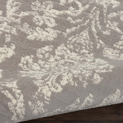 Taupe and ivory patterned rug with damask design, plush texture, edge resting on dark wood floor.