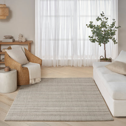 Bright neutral living room with light gray striped woven rug, cream sofa, wicker chair, potted tree and sheer curtains.