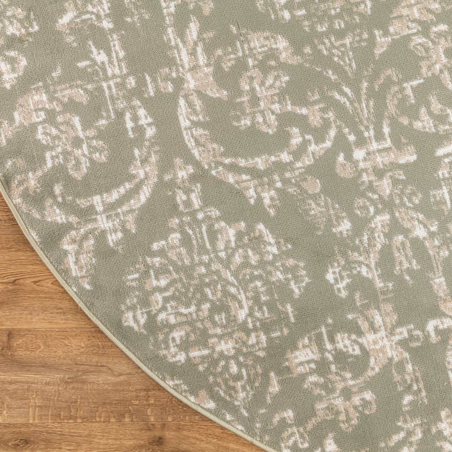Sage-green damask rug with distressed white motif, curved edge, woven texture on wood floor.