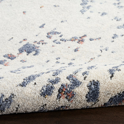 Cream rug with blue-gray & rust blotches; plush textured pile, rolled edge on wooden floor.