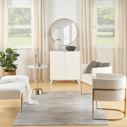 Bright minimalist living room with a rug, white cabinet, beige curtains, potted plant, and white lounge chair with a gold frame.
