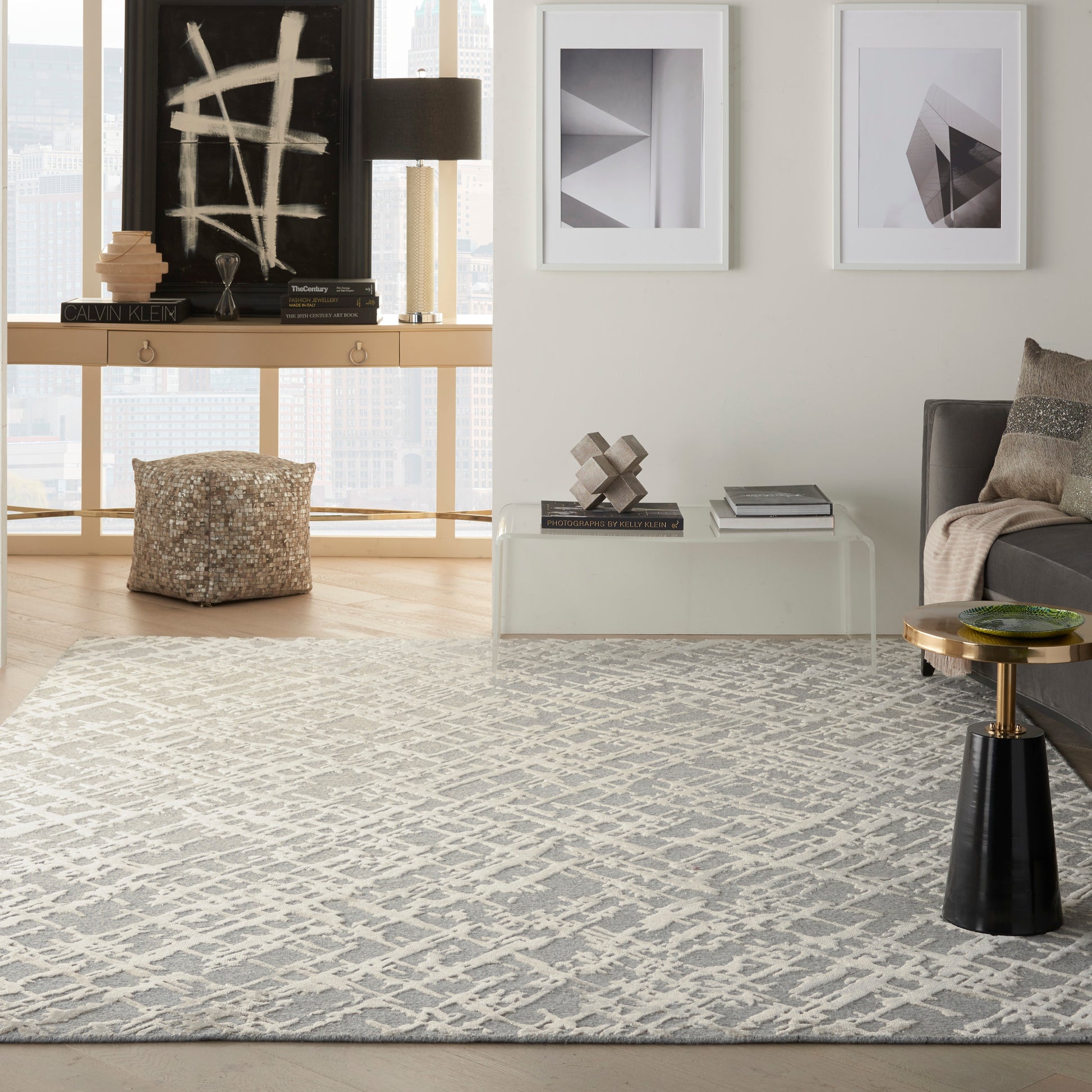 Modern living room with a gray geometric rug, glass coffee table, gray sofa, white-framed abstract art, sculptural decor, city view.