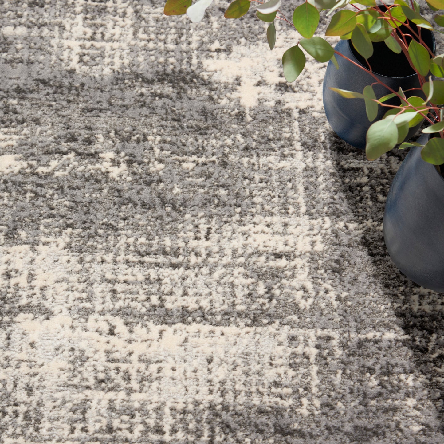 Gray and cream textured patterned rug with blue ceramic pots and green leafy plants along the edge.