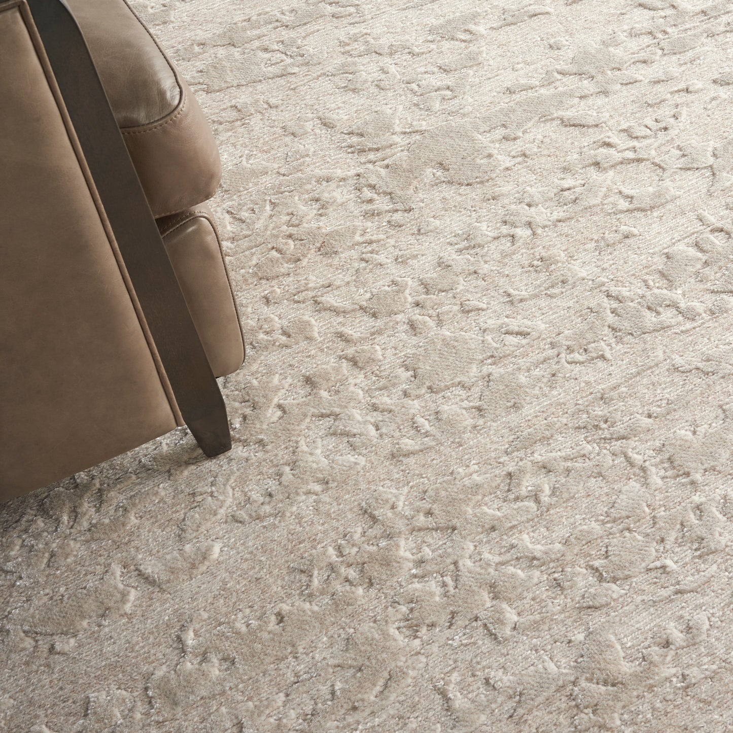 Beige leather sofa with dark wood legs on a light textured shag carpet.