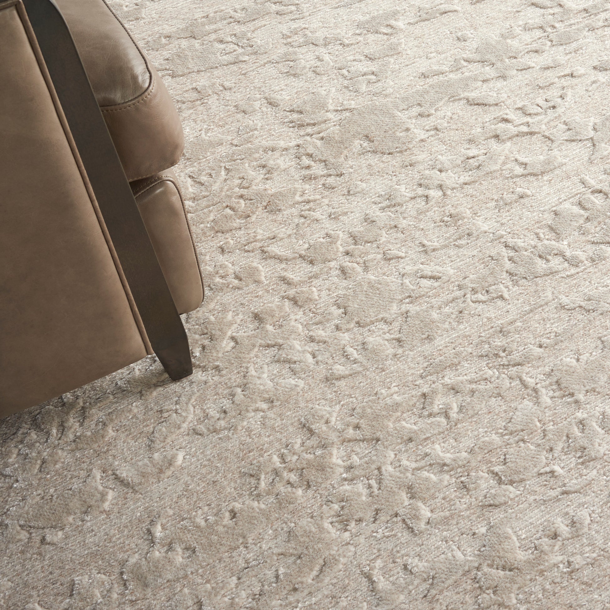 Beige leather sofa with dark wood legs on a light textured shag carpet.