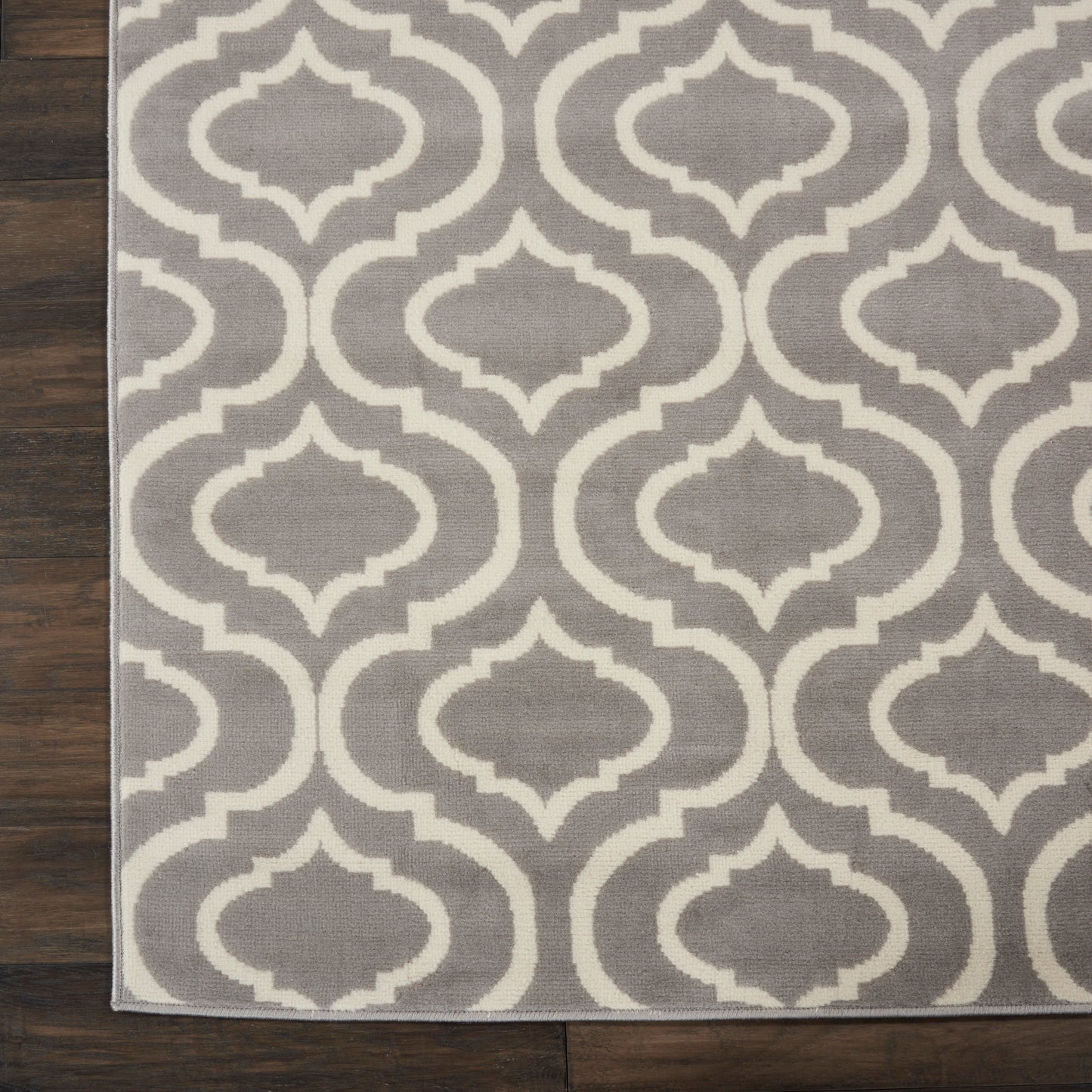 Grey and ivory trellis-pattern rug with repeating geometric shapes on dark wood floor.