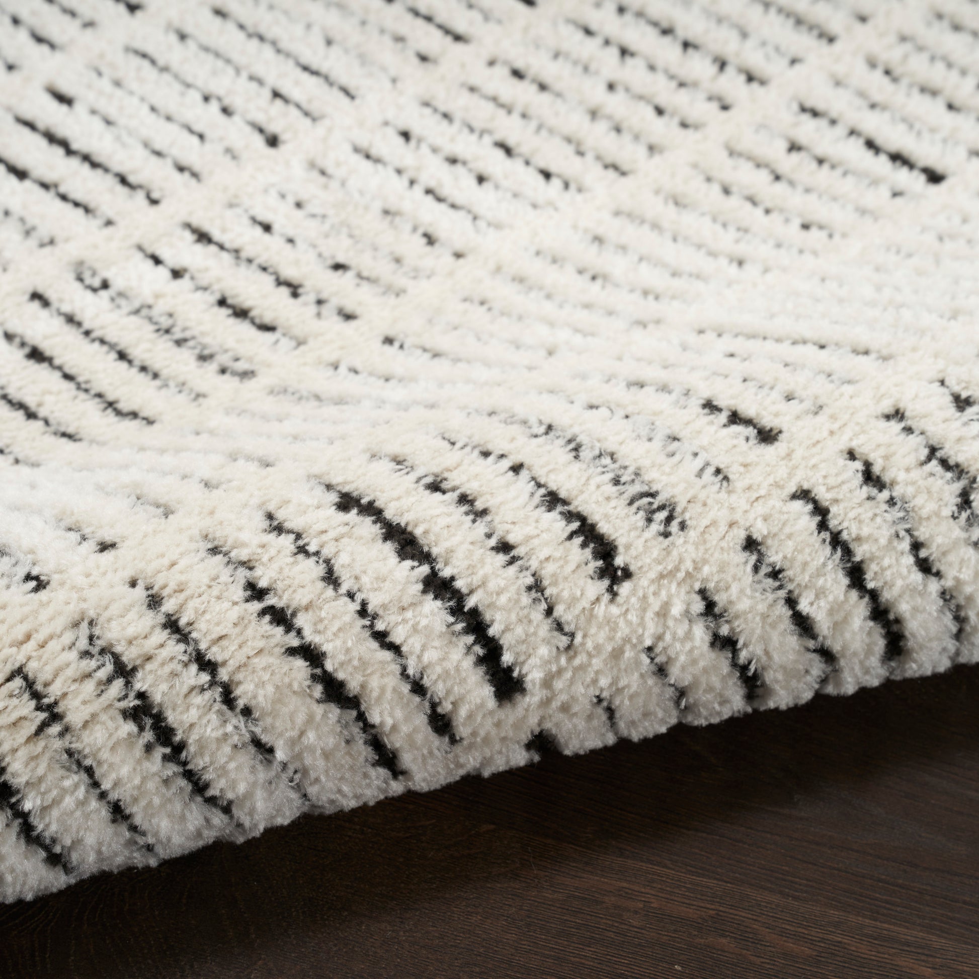 Cream looped rug with plush pile and subtle black linear stripes on a dark wooden floor.
