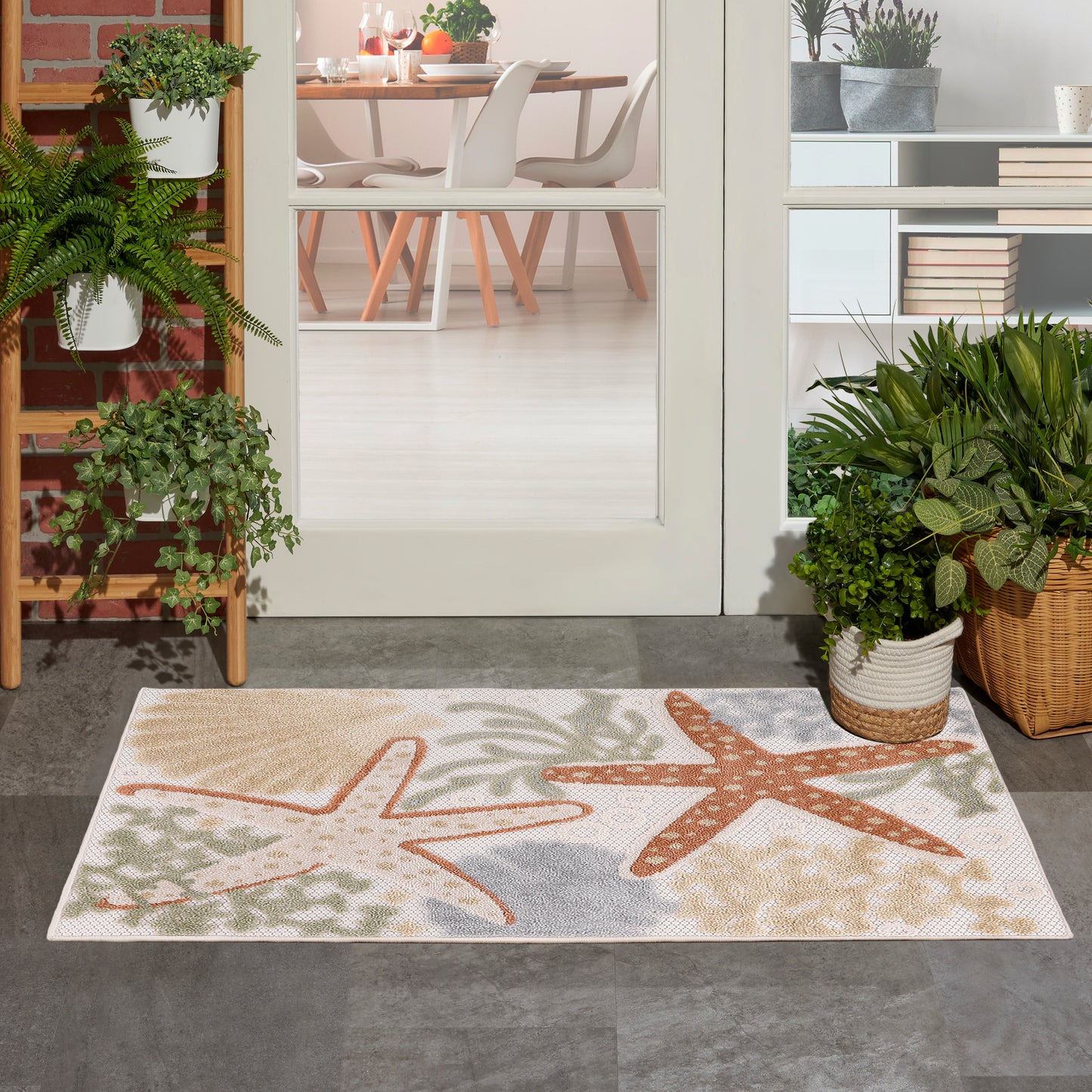 Outdoor rug with beach-themed orange and beige starfish designs on a light gray background at a doorway flanked by potted plants.
