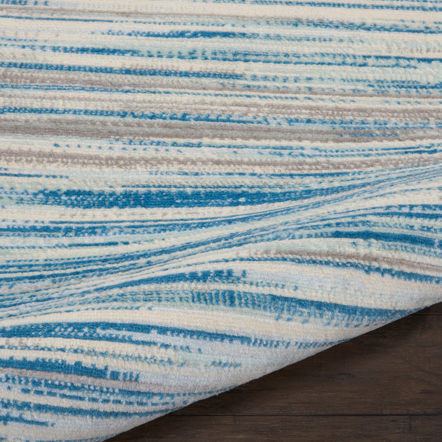Blue & cream abstract striped area rug with soft pile, folded corner on dark wood floor.