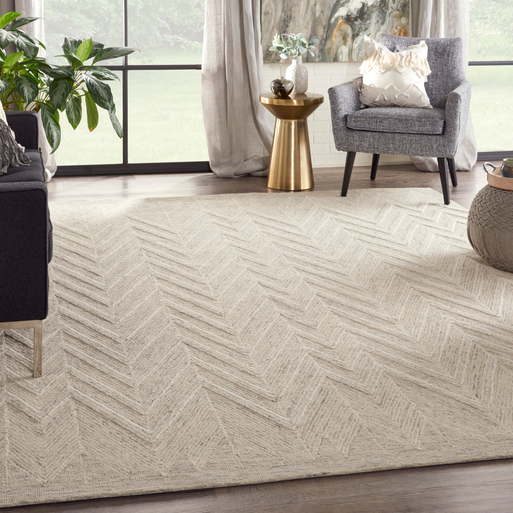 Beige chevron textured area rug in a bright living room with gray armchairs, a gold side table, and greenery.