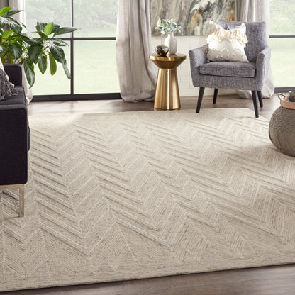 Beige chevron textured area rug in a bright living room with gray armchairs, a gold side table, and greenery.