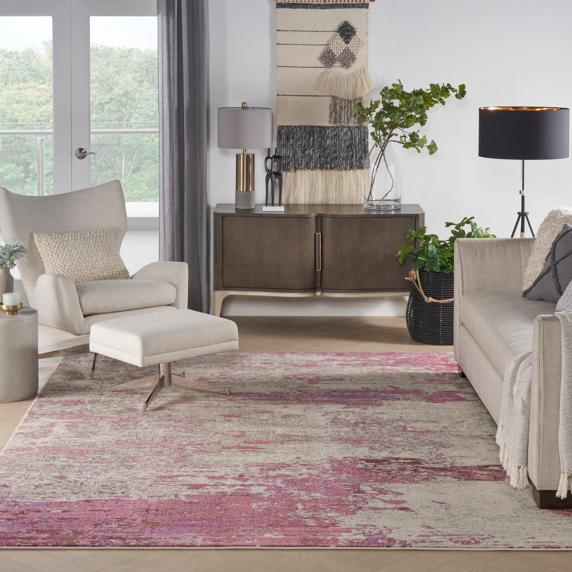 Living room with a pink-toned distressed area rug under beige sofa and ottoman, dark wood cabinet, plants, and modern lamps.
