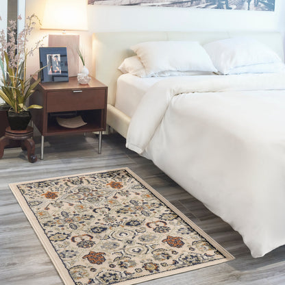 Beige floral area rug (3' x 5') in a bedroom scene with an ivory bed, white duvet and pillows, dark wood nightstand with lamp, plant, and framed photo.