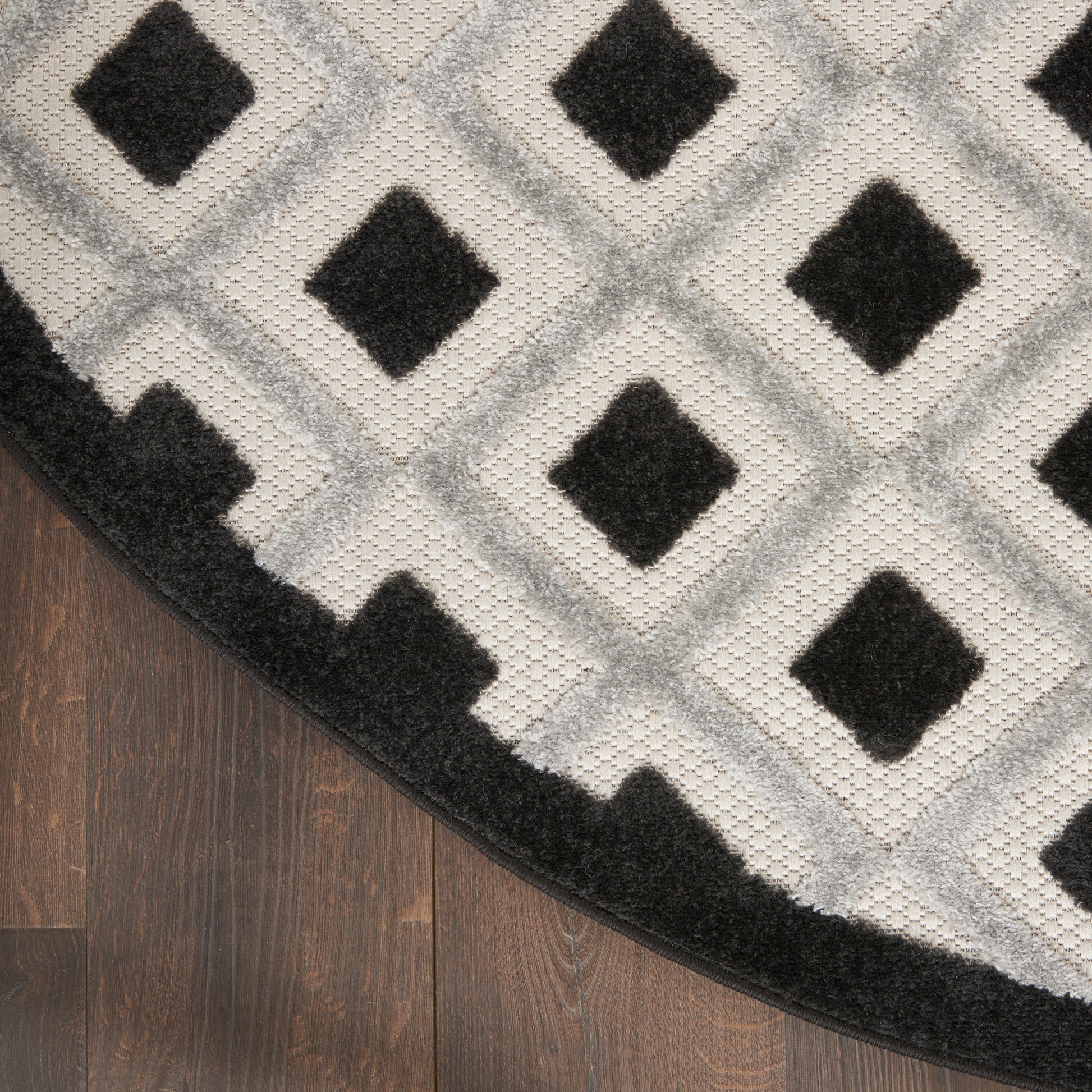 Round gray rug with diamond lattice pattern and black diamond centers, edged in black on a dark wood floor.