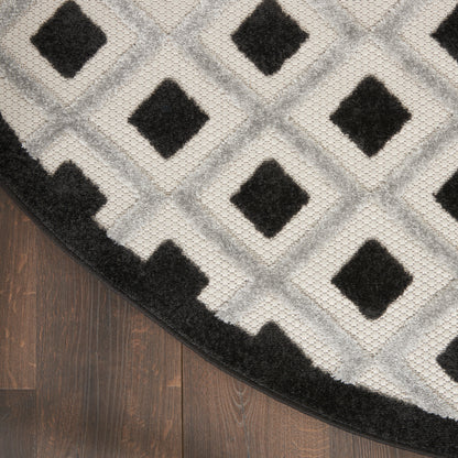 Round gray rug with diamond lattice pattern and black diamond centers, edged in black on a dark wood floor.