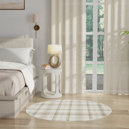 Bright neutral bedroom with white bedding, round white side table, wooden ring-base lamp, plaid beige rug, sheer curtains.