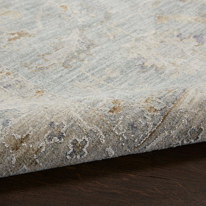 Distressed gray-beige oriental area rug with subtle blue and brown accents; plush pile, folded corner on dark wood floor.