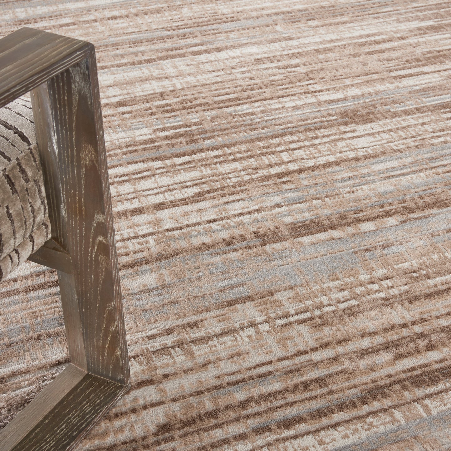 Textured tan-brown rug with a rustic wooden-framed chair resting on it.