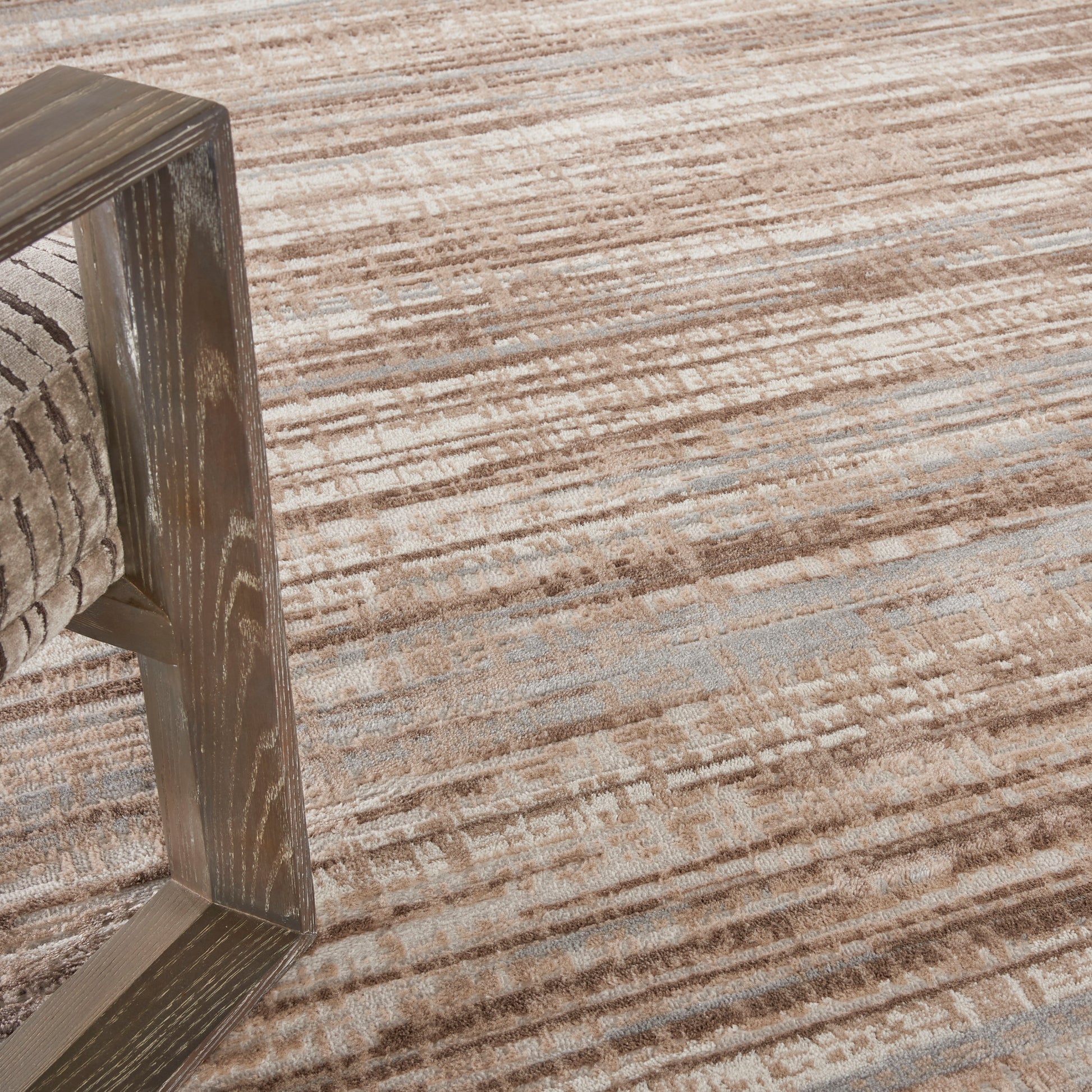Textured tan-brown rug with a rustic wooden-framed chair resting on it.