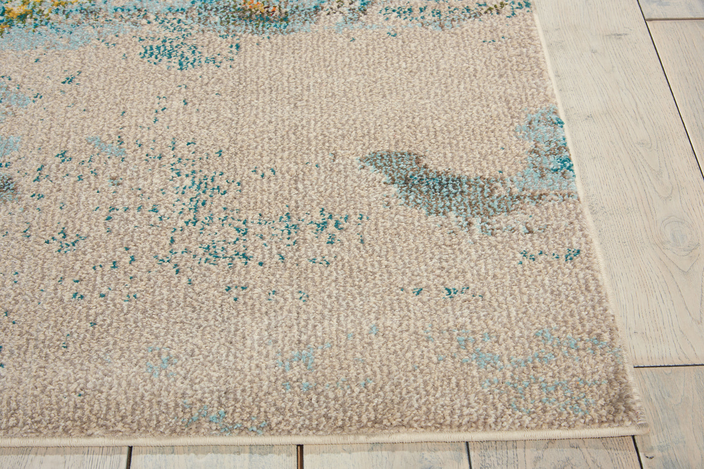 Rectangular beige woven rug with teal distressed pattern on light wooden floor.