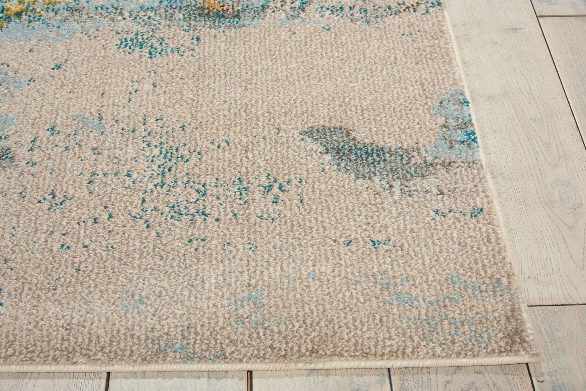 Rectangular beige woven rug with teal distressed pattern on light wooden floor.