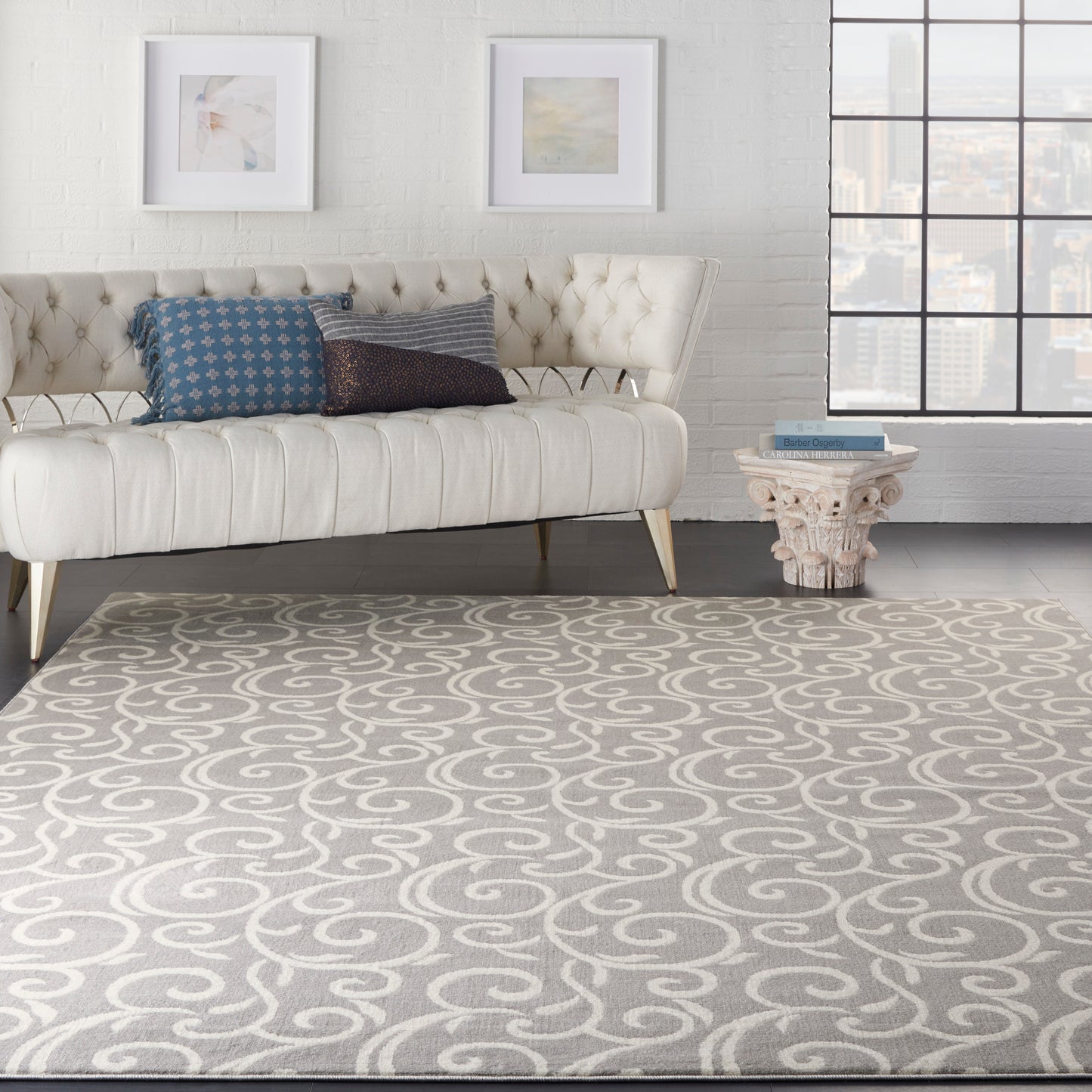 Cream tufted sofa with blue cushions, beige patterned rug, white brick wall, framed art, city-view window.