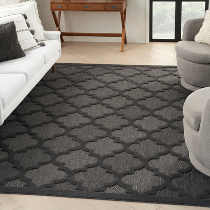 Dark gray geometric trellis rug on light wood floor in a modern living room with white sofa and gray chairs.