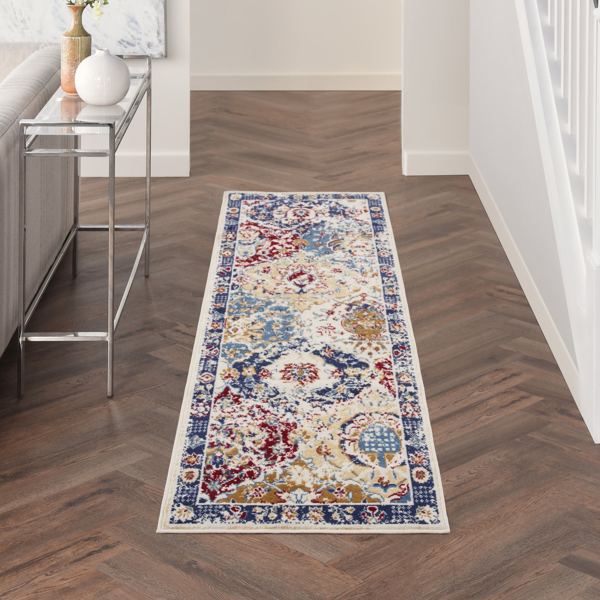 Long floral hallway runner rug in cream, blue, red and gold with a navy border on dark herringbone wood floor.