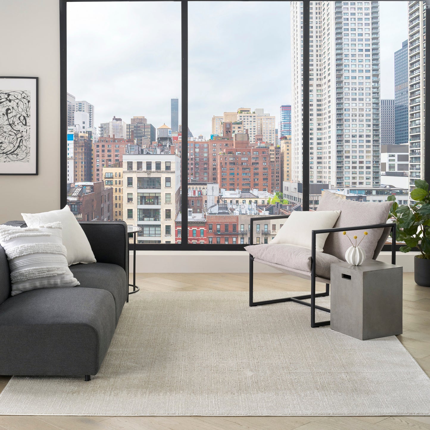 Contemporary urban living room with city view, dark gray sofa, beige rug, metal-framed chairs, concrete side table, plant.