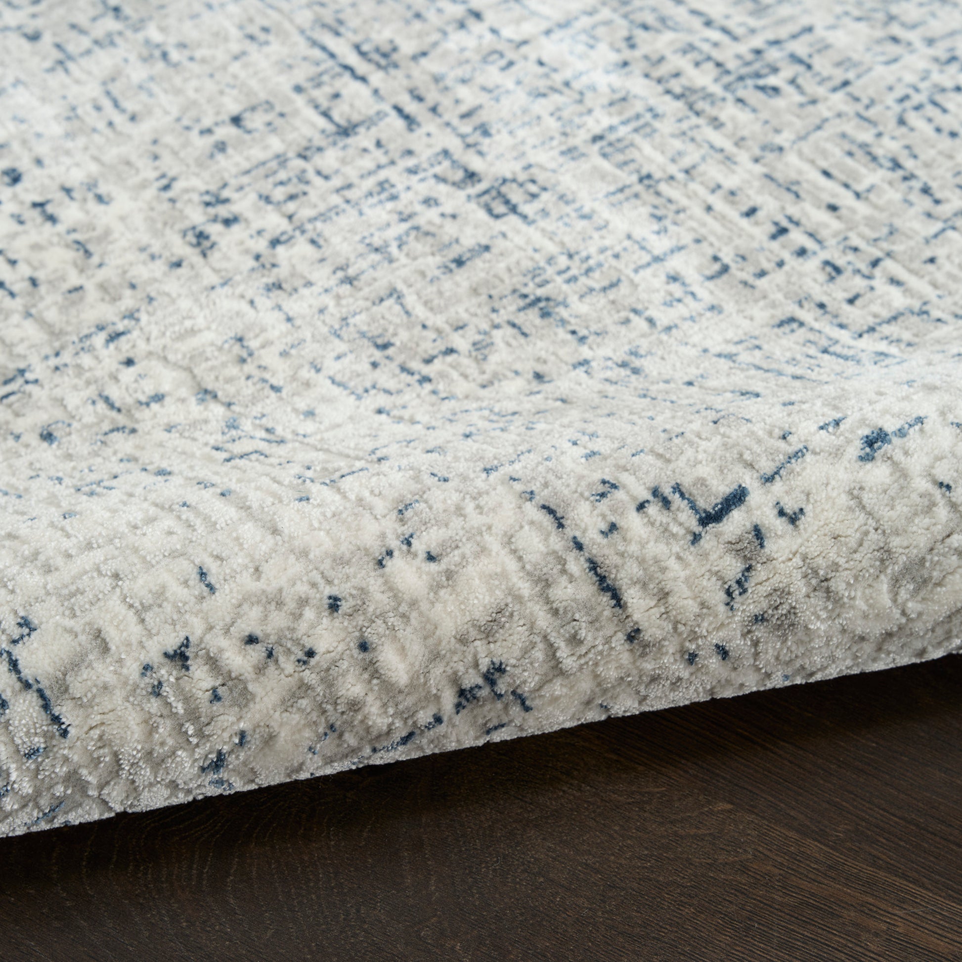 Rectangular ivory area rug with subtle blue abstract pattern; plush pile on dark wood floor.