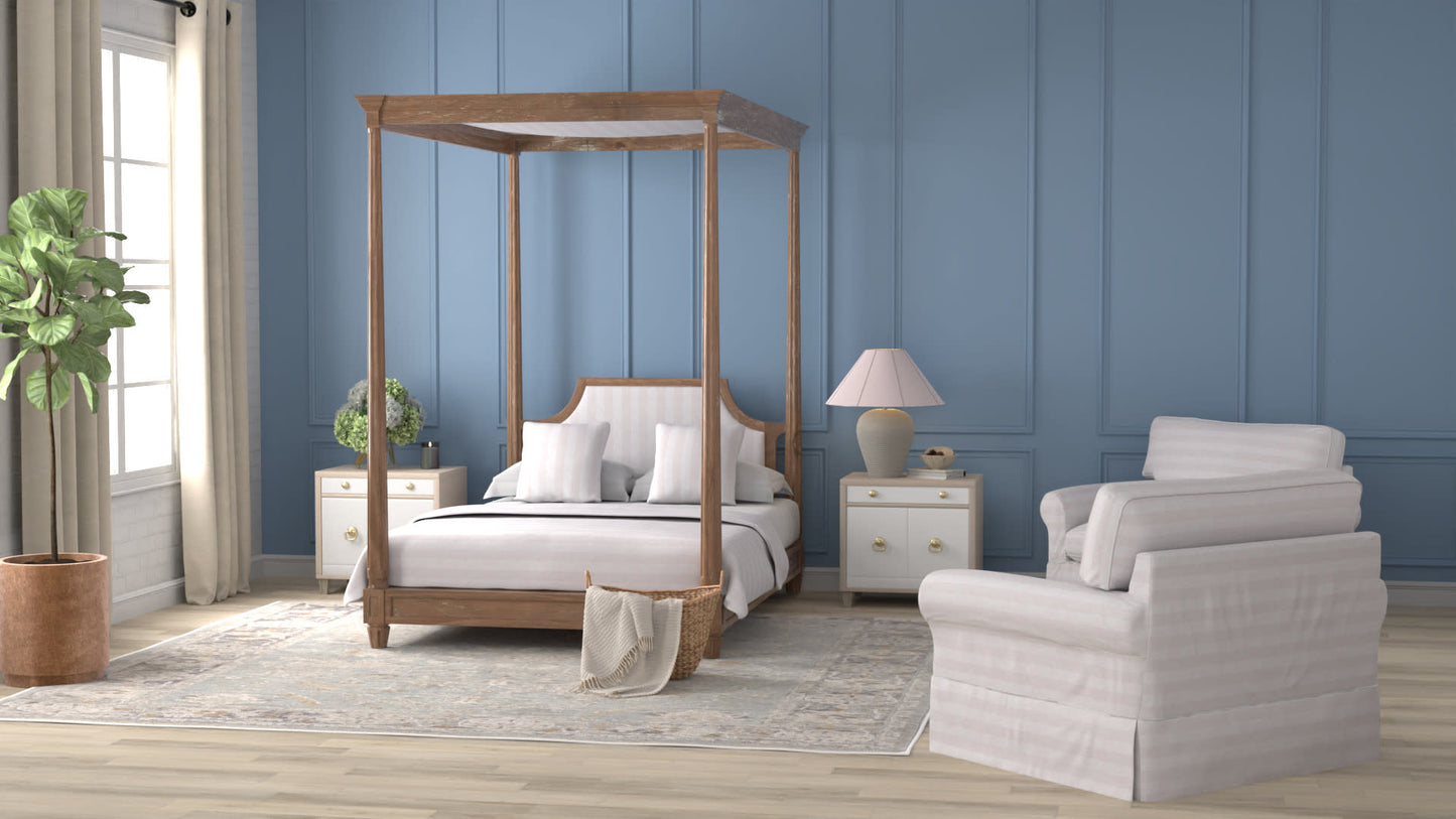 Wood four-poster bed with white bedding on blue paneled walls; two white nightstands, lamp, armchair & rug.