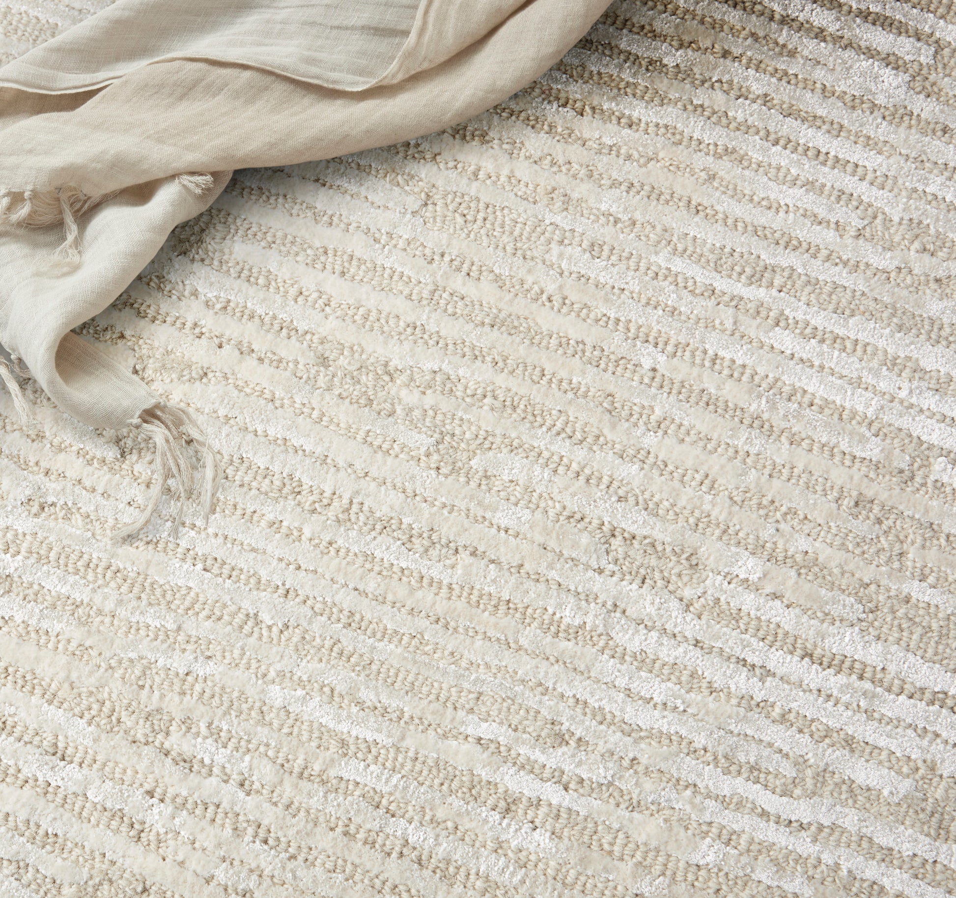 Cream and beige striped woven rug with soft, textured surface; light linen throw draped at corner.