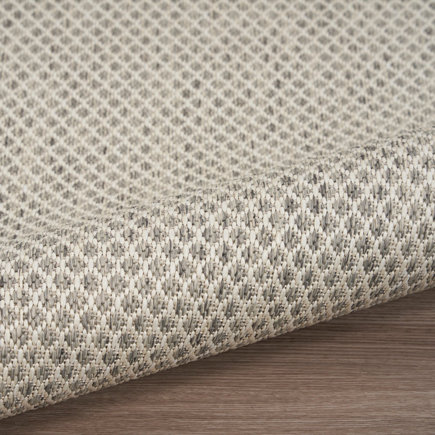 Beige and gray woven fabric rug with a subtle geometric texture, rolled on a wood floor.