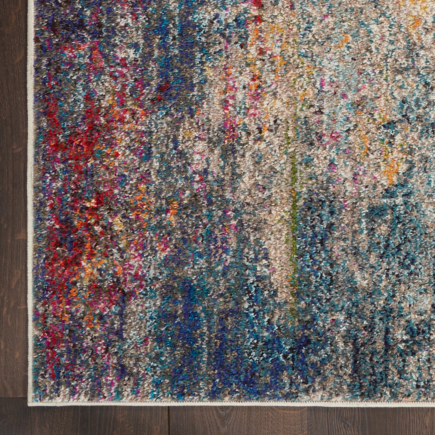 Shaggy, multicolored abstract area rug with blues, teals, reds and creams, cream border on dark wooden floor.