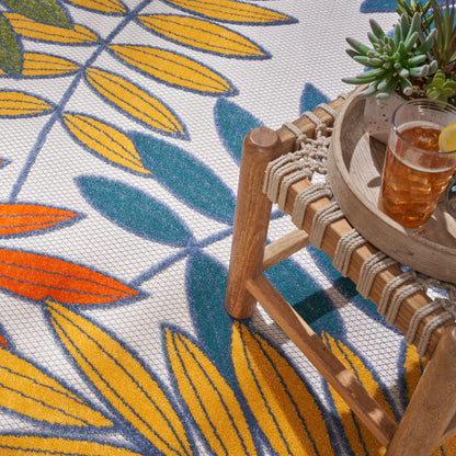 Round tropical rug with bright leaf pattern; wooden rattan coffee table with rope-wrapped sides on the rug; succulent plant and iced tea with lemon.