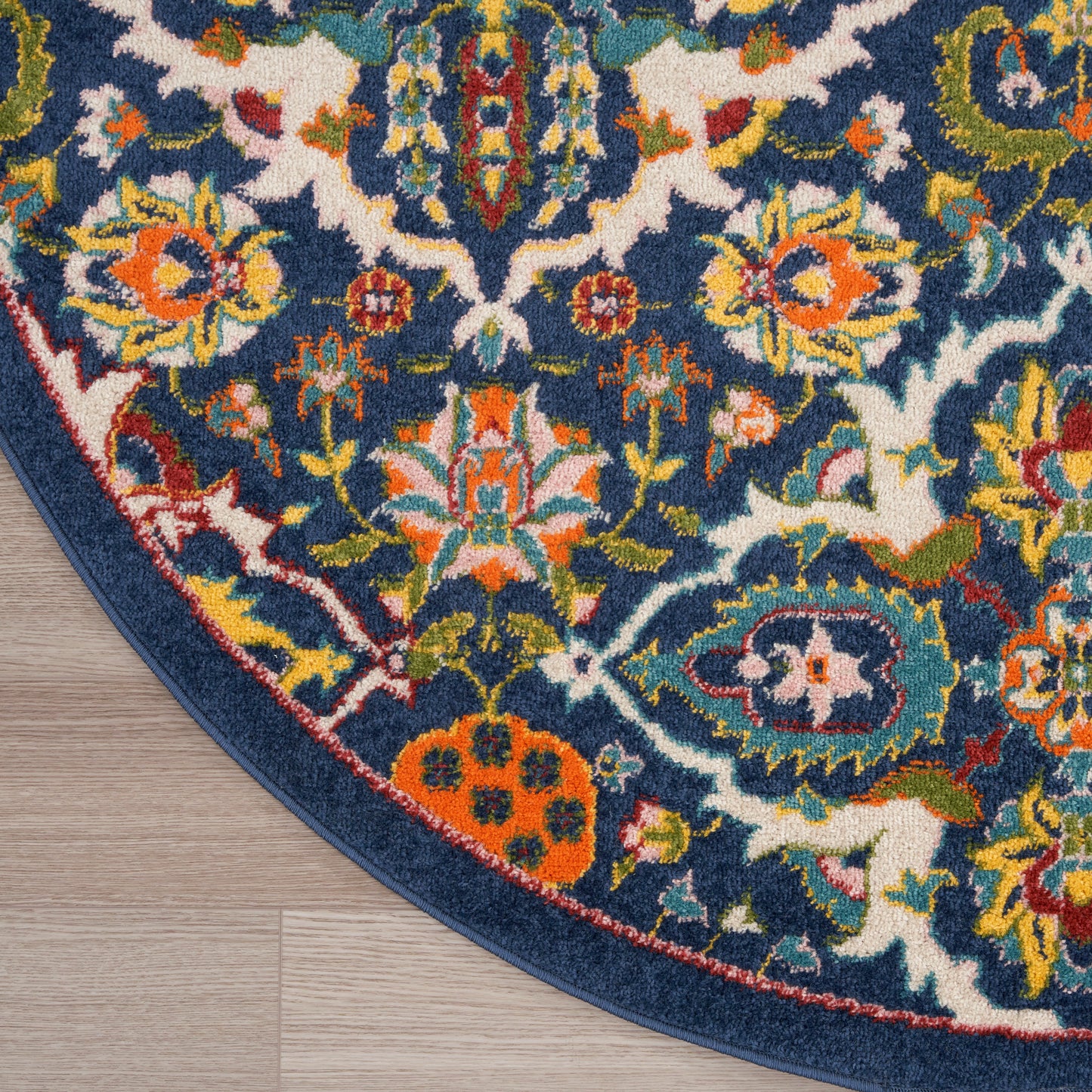 Round navy blue oriental rug with vivid floral motifs in orange, yellow, green and white; bound edge on wood floor.