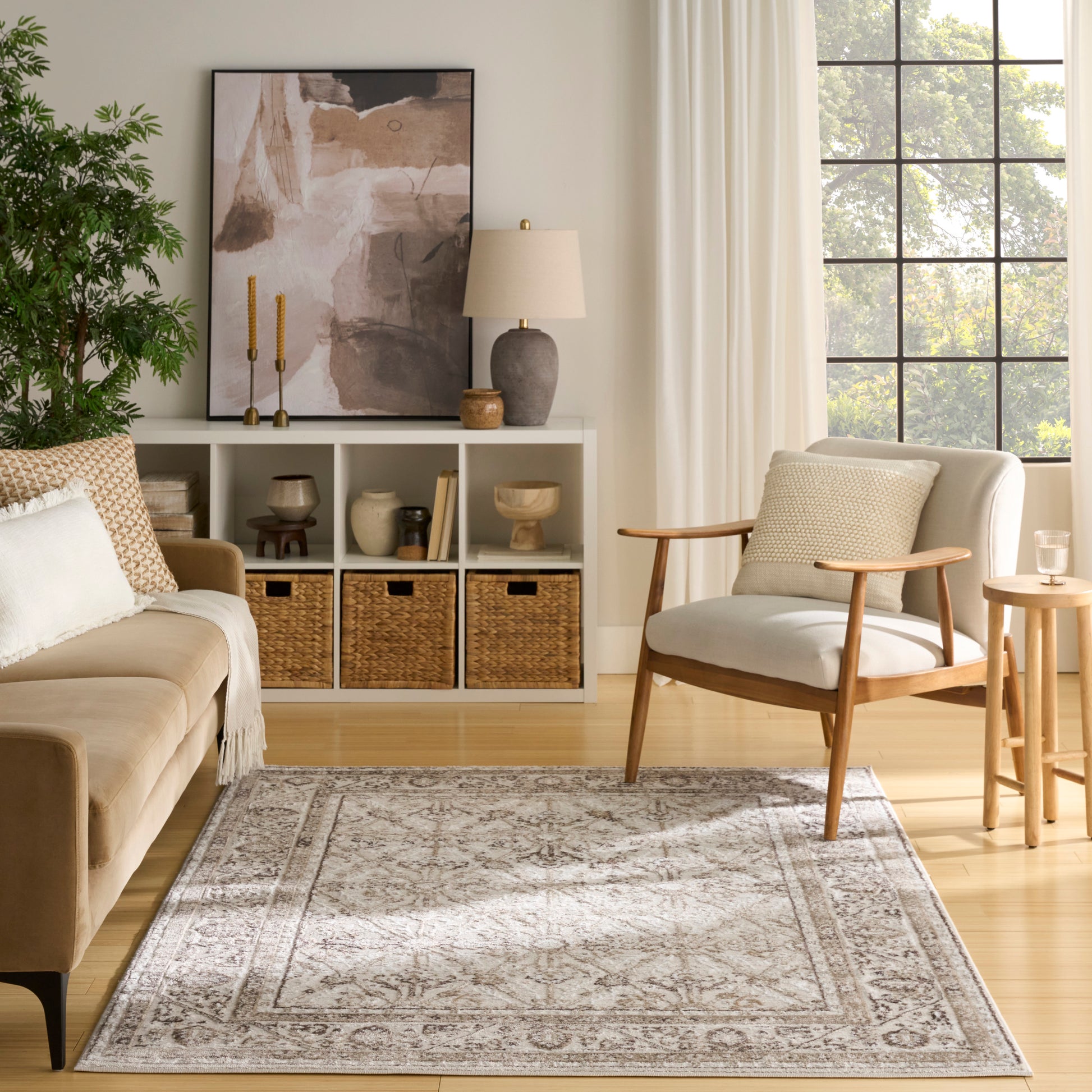 Cozy neutral living room with beige sofa, mid-century wood armchair, patterned rug, white cubby shelves and wicker baskets.