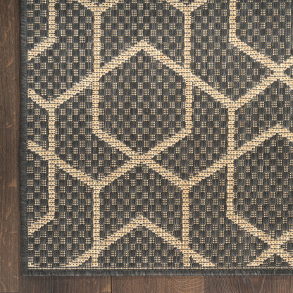 Charcoal woven rug with beige geometric lattice diamonds; textured weave and wood floor edge visible.