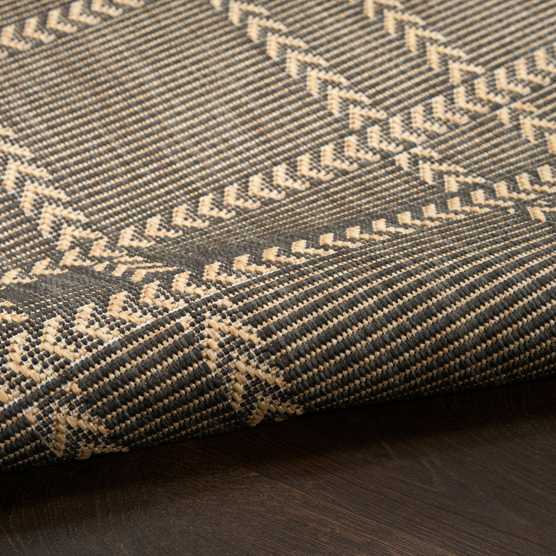 Brown and beige woven textile with chevron and herringbone patterns, folded on dark wood.