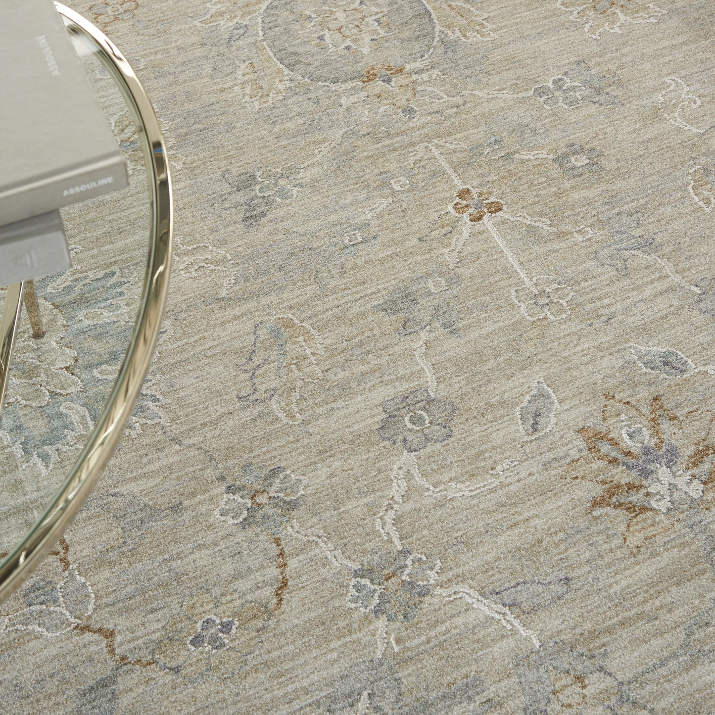 Beige floral area rug with muted blue-grey and brown motifs; round glass coffee table with a chrome frame.