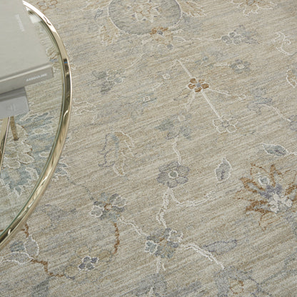 Beige floral area rug with muted blue-grey and brown motifs; round glass coffee table with a chrome frame.