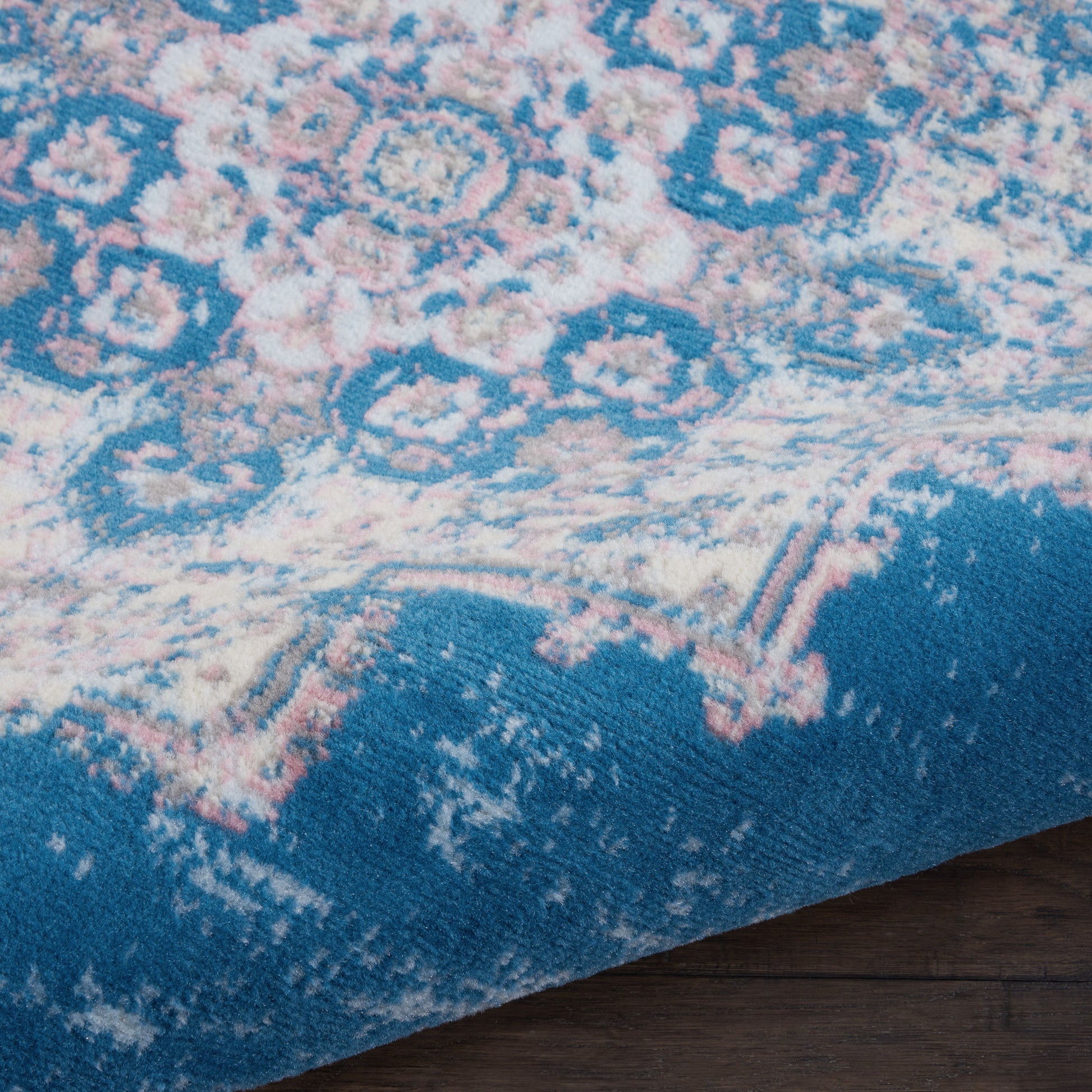 Blue oriental rug with pink and cream floral motifs, plush pile, close-up on a wooden floor.