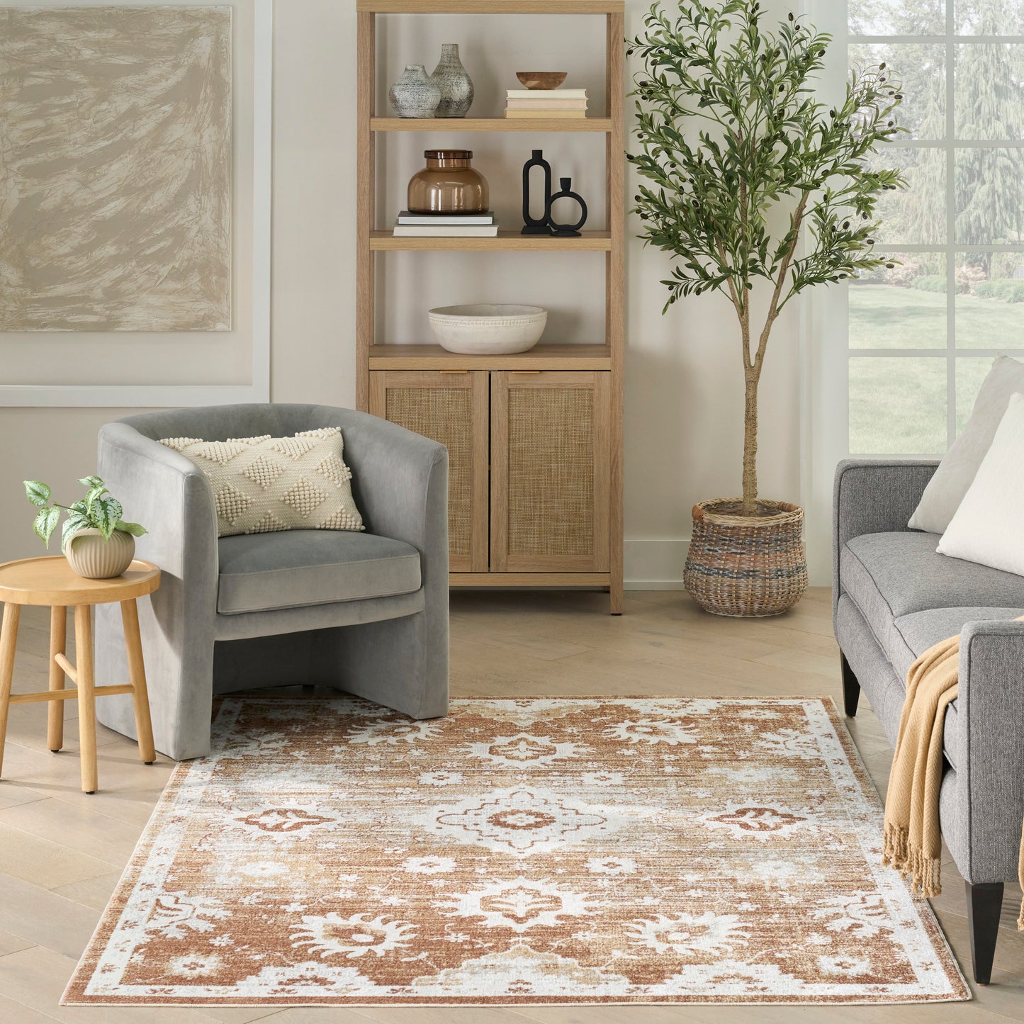 Cozy living room with a brown-and-white ornate rug, gray armchairs, light wood shelving, and a tall potted plant.