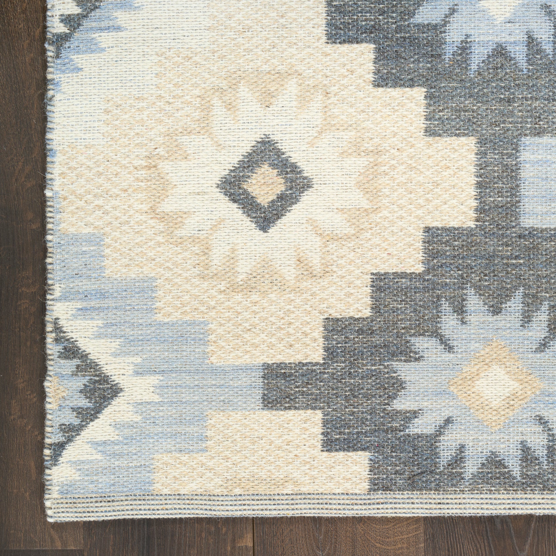 Kilim-style woven area rug with ivory sunburst center, navy and light blue geometric diamonds and stepped borders.